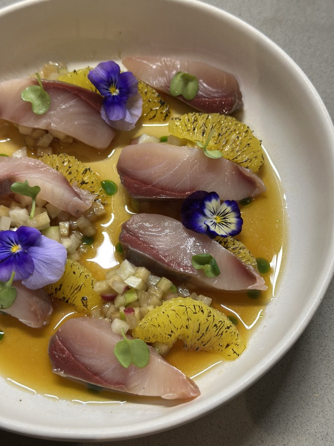 Slices of raw fish with citrus segments and violas in a pale broth